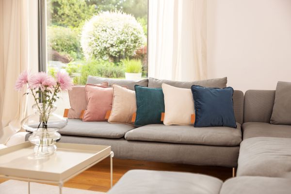 Das Bild zeigt ein Wohnzimmer. Auf dem Sofa ist das HK 77 Heaty Akku-Heizkissen in sechs Farbvarianten zu sehen.Ein Wohnzimmer