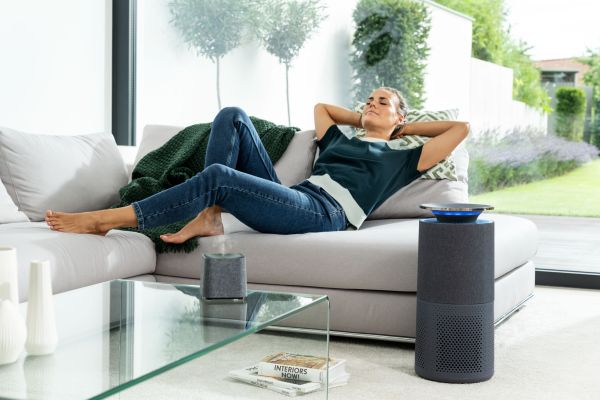 A woman is lying relaxed on a sofa, in front of which stands the Beurer LR 401 air purifier.