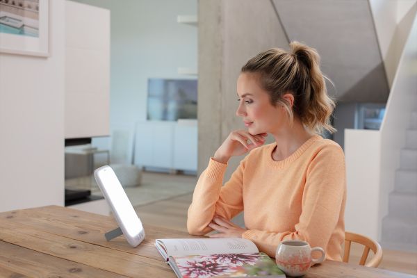 A woman is sitting at a table and using the TL 35 daylight lamp.