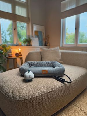Das Massagegerät „Buddy" und das Wärmebett "Kira" liegen auf einem beigen Sofa.