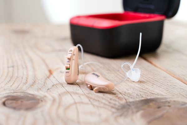 On a table lie the HA 90 digital hearing aid and the charging and transport station.
