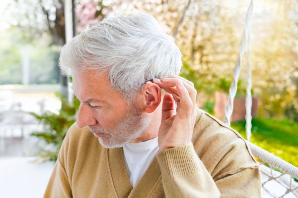 A man with grey hair reaches behind his ear, the hearing aid HA 90 digital can be seen there.