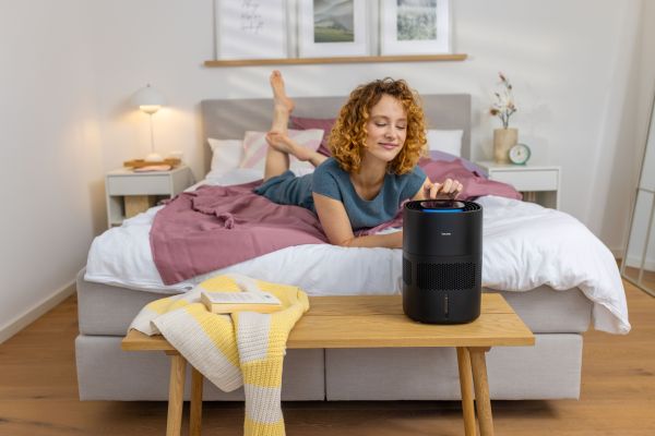 Rothaarige Frau liegt auf dem Bett und verwendet den Beurer LB 100