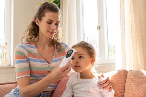 Eine Frau misst bei einem kleinen Mädlichen Fieber mit einem kontaktlosen Stirnthermometer
