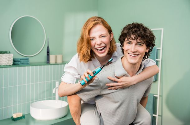 Eine Frau und ein Mann in einem grünen Badezimmer mit einer Schallzahnbürste von Beurer