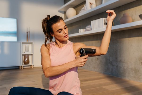 Eine Frau nutzt die Massage Gun MG 195 am Oberarm.