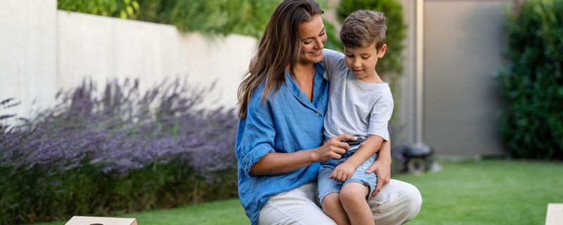 Mujer en el jardín tiene a su hijo en el regazo y trata su picadura de insecto con el calmador de picaduras de insectos Beurer BR 90