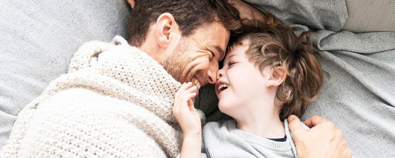 Padre e figlio sdraiati testa a testa, coccolati a letto e si guardano ridendo