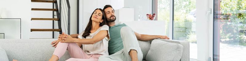 Una pareja está sentada abrazada y con los ojos cerrados en el sofá de la sala
