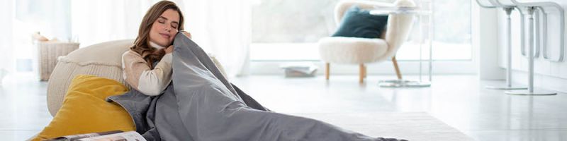 Jeune femme assise détendue dans le salon et se blottit avec la couverture chauffante Beurer HD 75