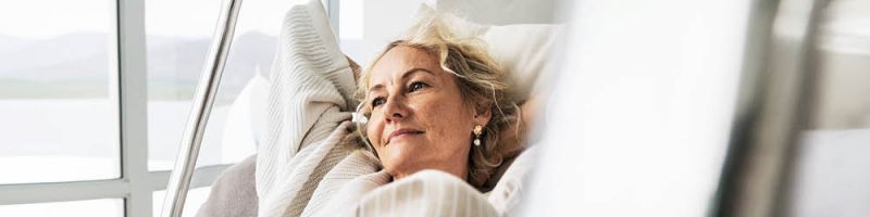 Una donna anziana è seduta su una poltrona e guarda con un'espressione serena fuori dalla finestra