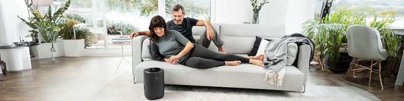 Pareja de mediana edad acostada en el sofá y el humidificador Beurer LB 200 en primer plano