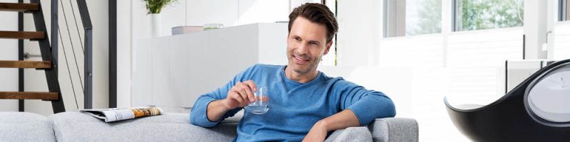 Hombre de mediana edad sentado en un sofá con un vaso de agua en la mano
