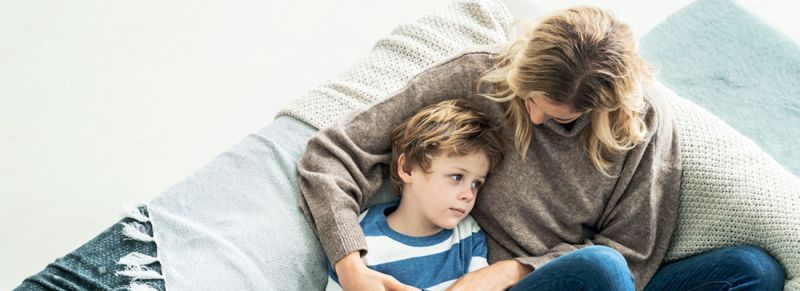 Fils dans les bras de sa mère. Ils sont assis sur le canapé et la mère regarde le garçon.