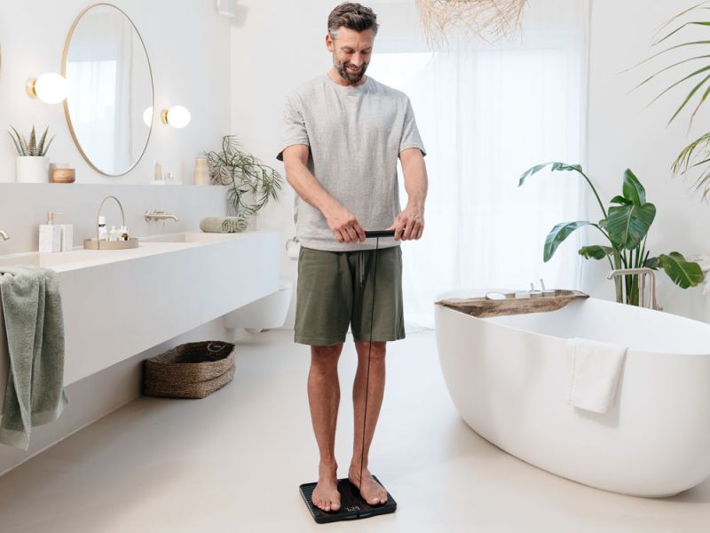 Un uomo di mezza età misura i propri parametri corporei nel bagno con la bilancia diagnostica BF 990. 