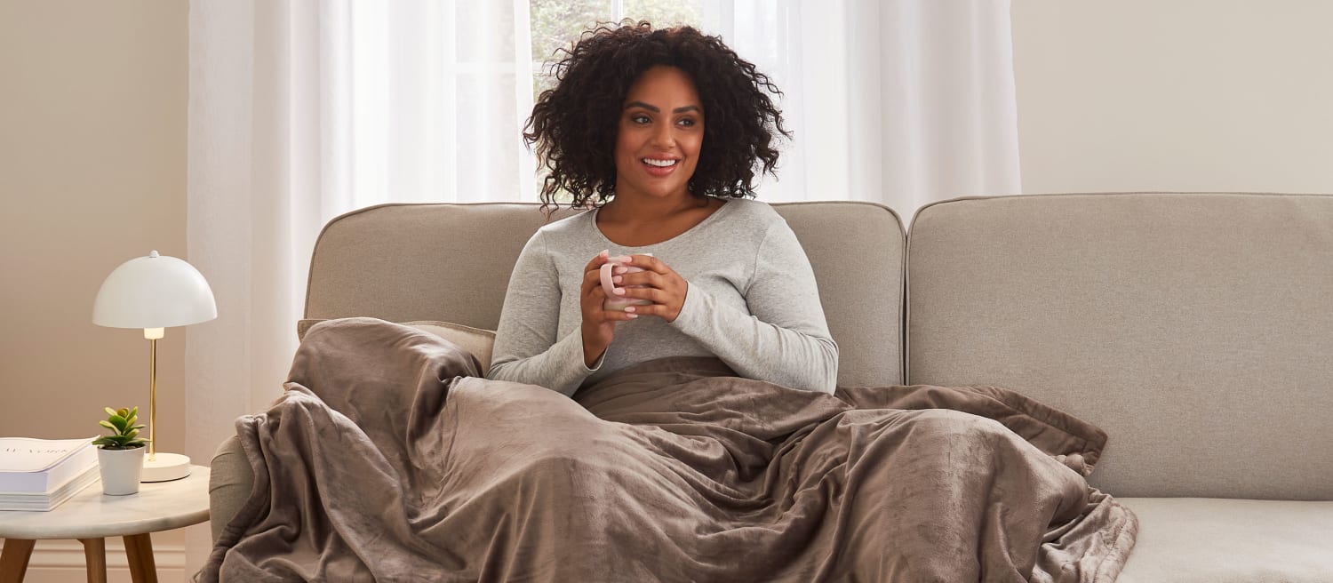Woman enjoys warmth of heating blanket on sofa