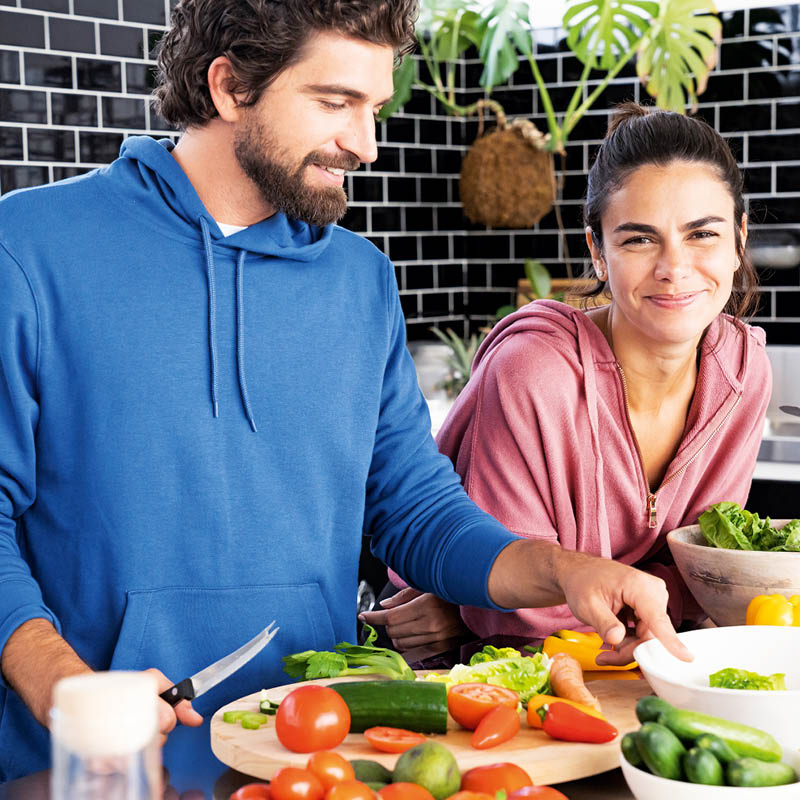 Hombre y mujer preparando juntos verduras frescas en una cocina moderna y riendo