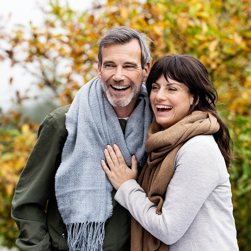 Un couple d'âge moyen, bien emmitouflé, se tient joyeusement dans les bras l'un de l'autre. Ils sont dans la nature