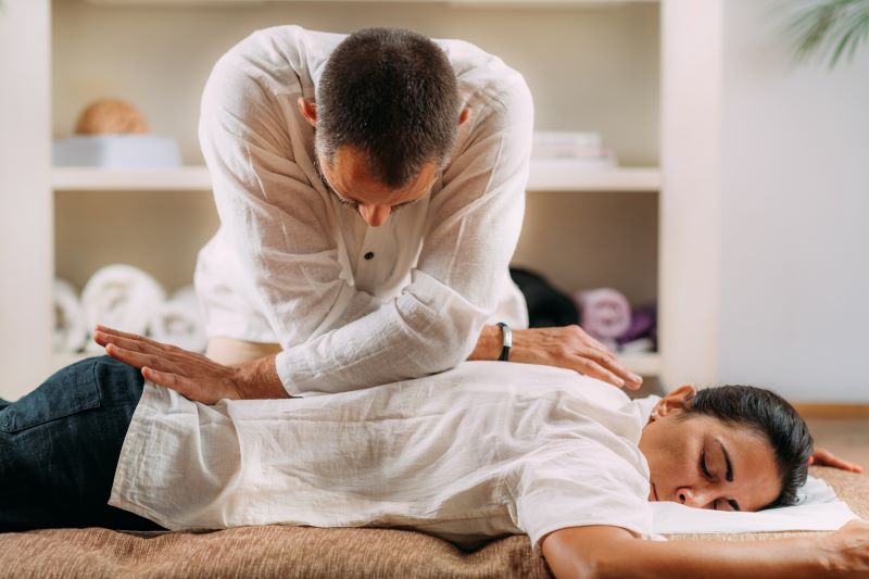 Terapeuta dà un massaggio Shiatsu a una donna vestita e applica una pressione mirata con il suo peso corporeo sulla sua schiena