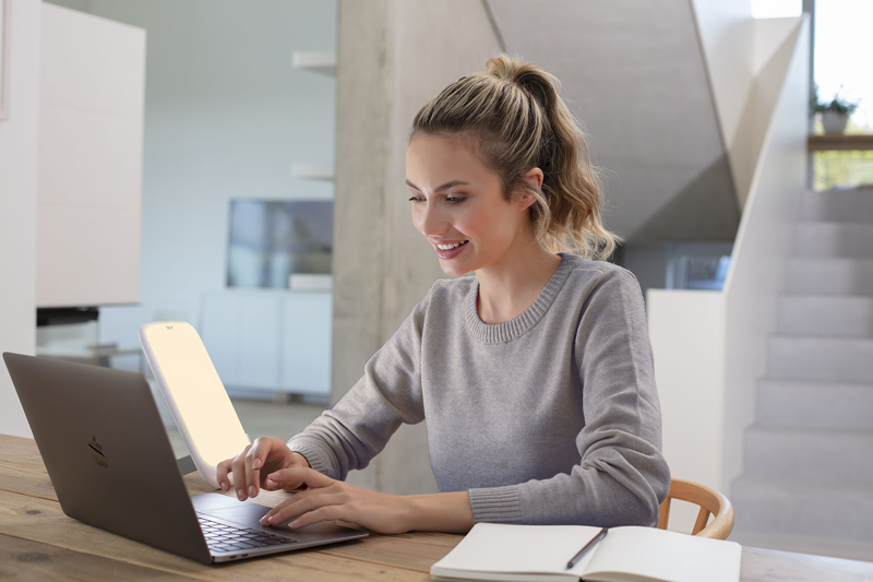 Femme travaillant à domicile sur son ordinateur portable et utilisant la lampe de luminothérapie Beurer TL 35