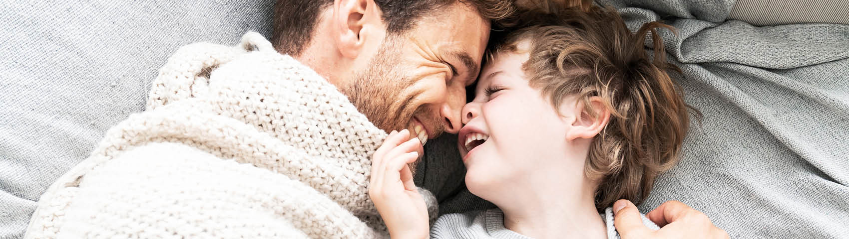 Père et fils se blottissent sous une couverture dans le lit et se regardent en riant