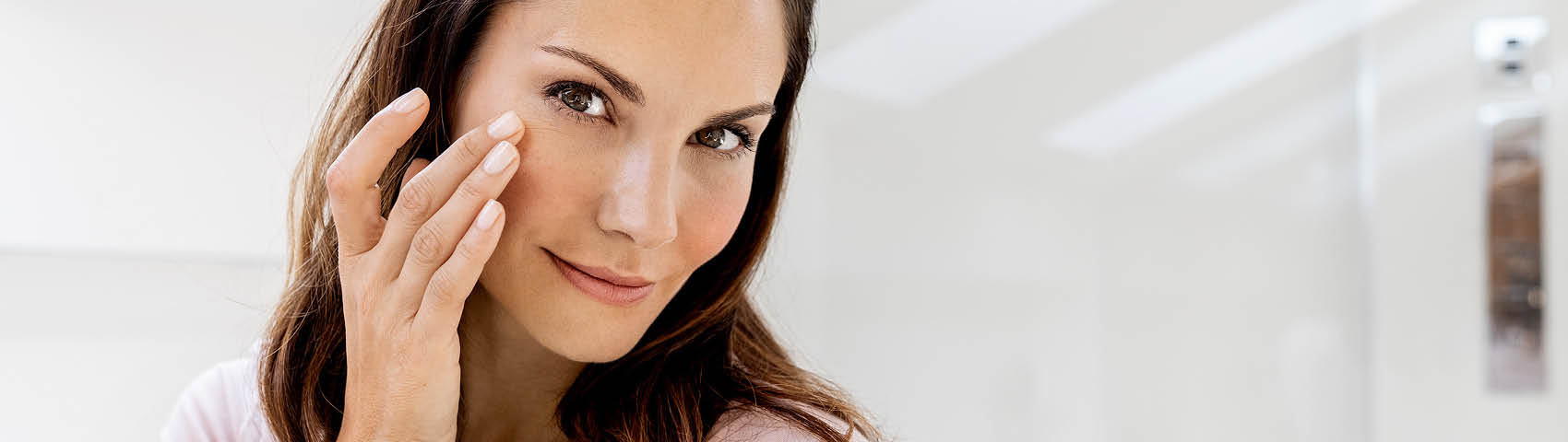Mujer de mediana edad aplicándose crema facial en el rostro y sonriendo