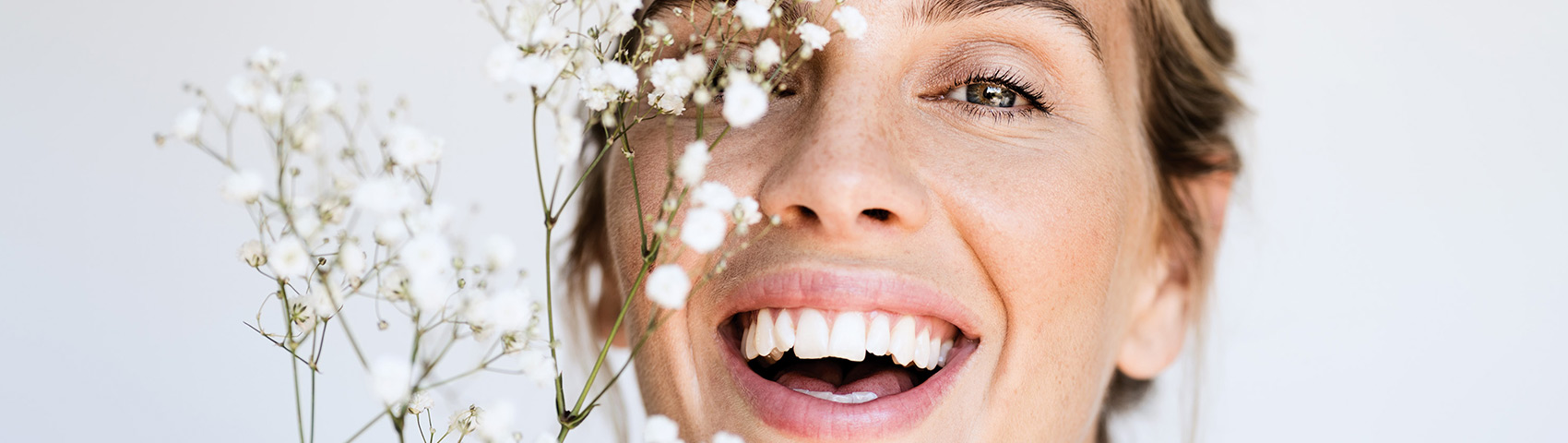 Jeune femme souriant à la caméra, des petites fleurs blanches devant son visage