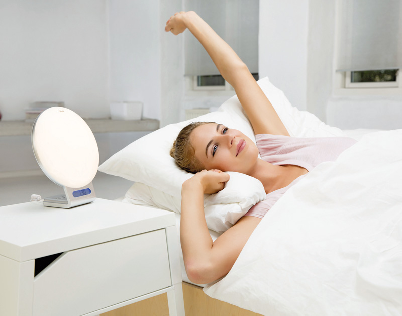 Una donna si sveglia rinfrescata a letto con la sveglia luminosa Beurer WL 75