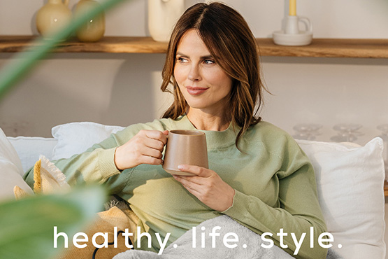 A dark-haired woman sits on a sofa with an electric blanket. Accompanied by the Beurer brand claim healthy. life. style. A dark-haired woman sits on a sofa with an electric blanket. Accompanied by the Beurer brand claim healthy. life. style.